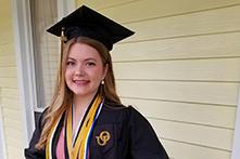 image of Annie Fuelle standing on a porch in her graduation cap and gown