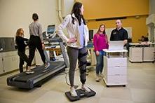 A woman walking on a treadmill, another woman standing on a scale, while students perform fitness evaluations.